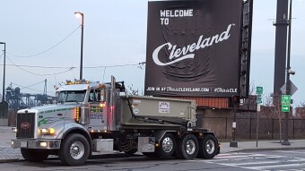 A roll off container truck posing in front of a Welcome to Cleveland sign